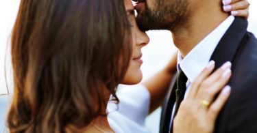 man kissing woman on her forehead