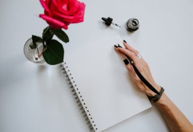 person holding red rose and white spiral notebook