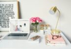 MacBook Air beside gold-colored study lamp and spiral books