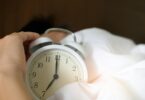 A close-up of a hand reaching for a ringing alarm clock, symbolizing waking up in the morning.
